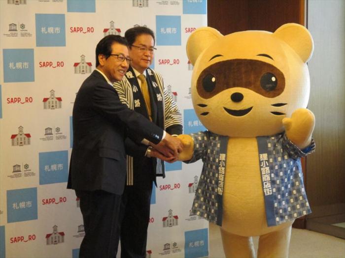 秋元市長と島口理事長様とだっこポンの三名が握手する写真