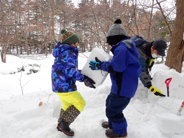 雪のブロックを一緒に運ぶ子どもたち