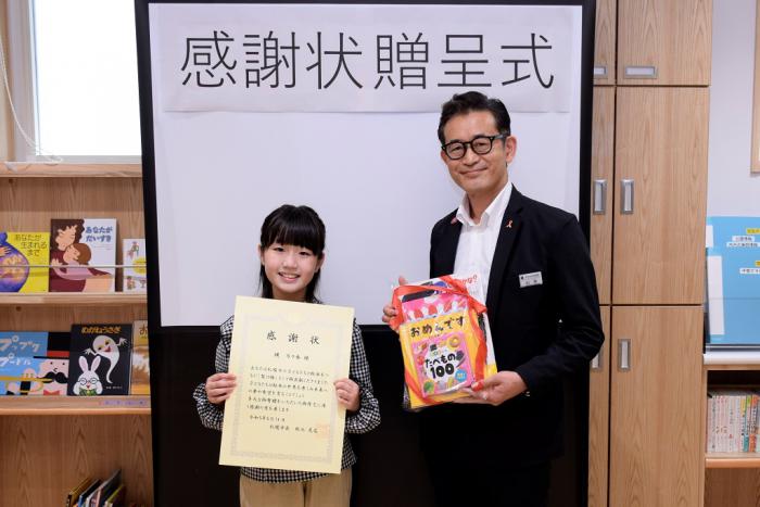 感謝状を手にする縄さん（左）と寄付された絵本を手にする山本局長（右）