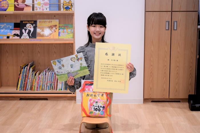 感謝状と自身の作品を手にする縄さん
