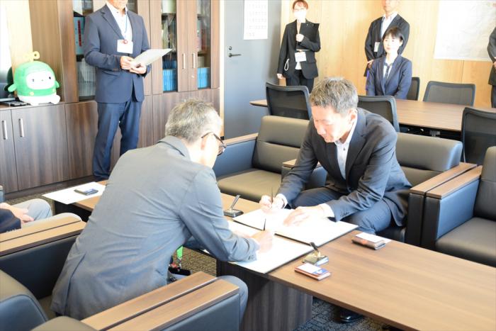 覚書にサインをする久道区長（左）と八並代表取締役社長（右）