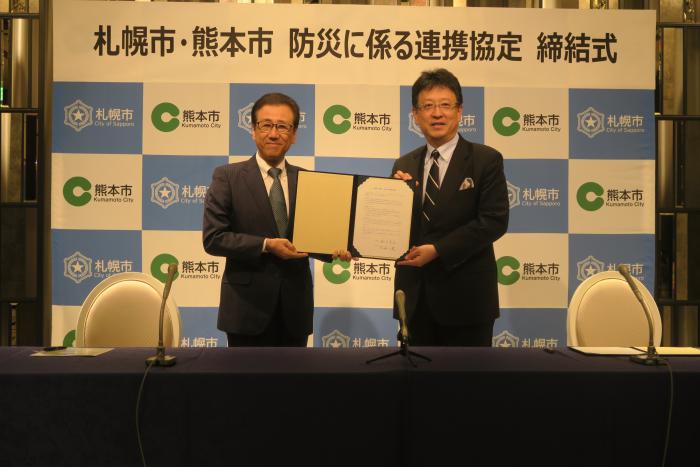 札幌市長と熊本市長で協定書を掲げている写真