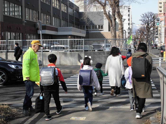 交通安全指導員に見守られて横断歩道を渡る児童たちの様子