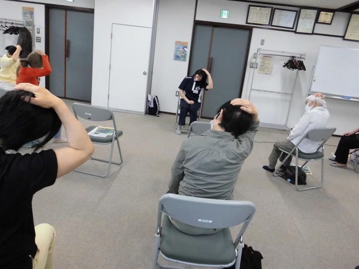 椅子に座った状態で参加者たちが首のストレッチをしている様子
