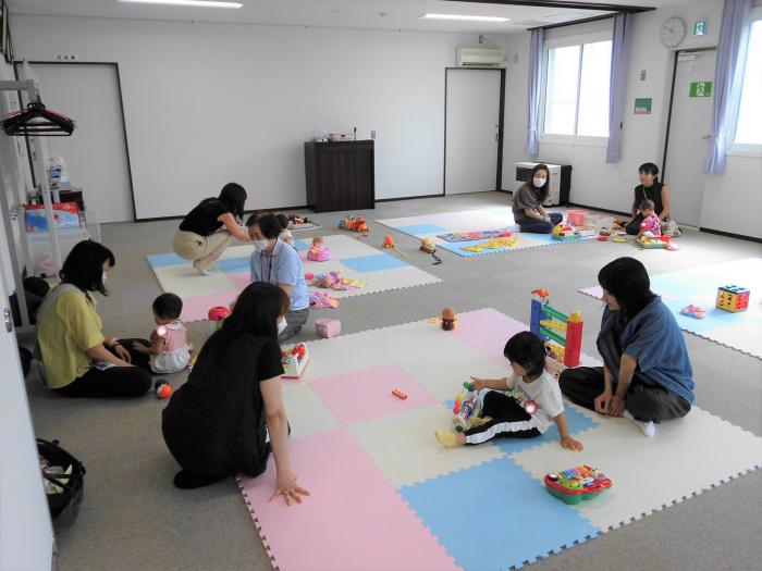 床に敷いたマットに座って遊んでいる4組の親子