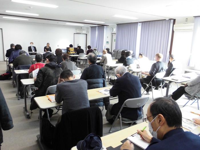 前方に議長が着席し、向い側に多くの出席者が着席している会議場の様子