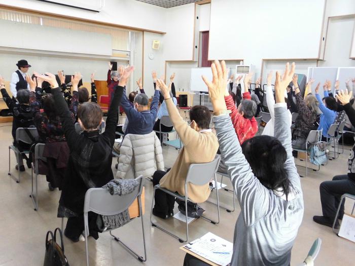 演奏に合わせて参加者が椅子に座りながら体を伸ばす運動をしている様子