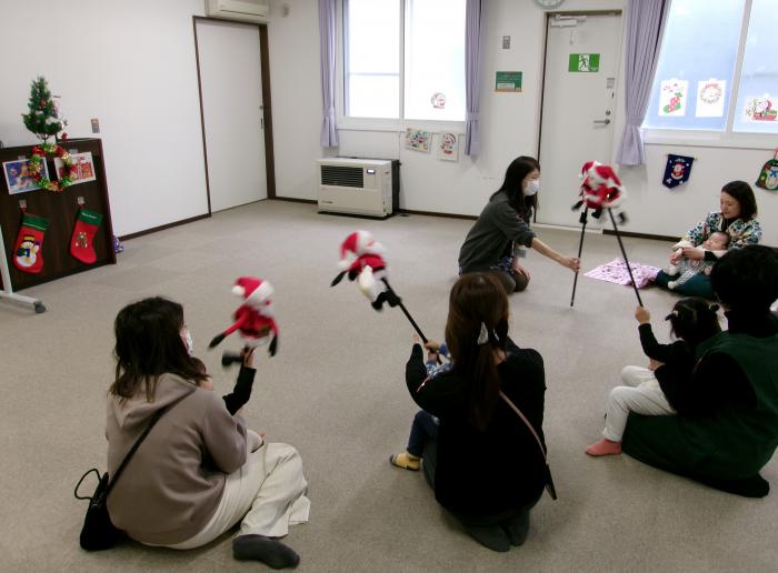 親子たちが音楽に合わせてサンタクロースの棒人形を振っている様子
