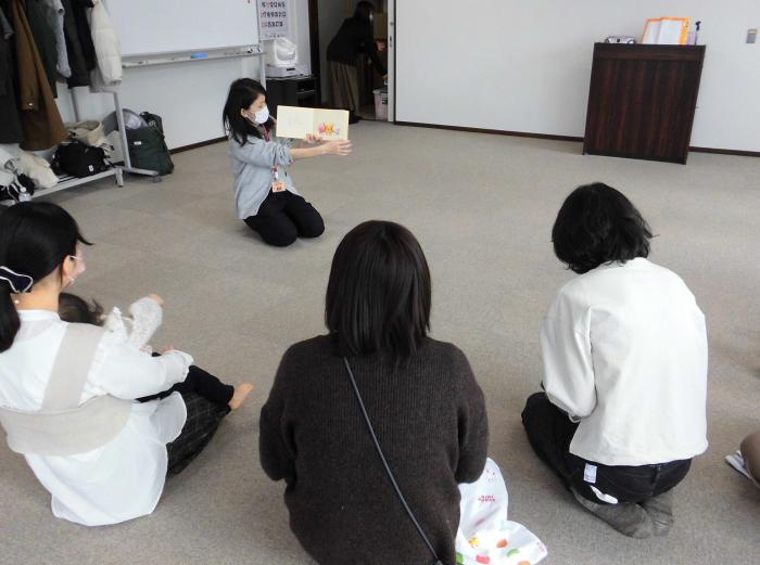 親子が絵本の読み聞かせをしている人を囲んで聞き入っている様子
