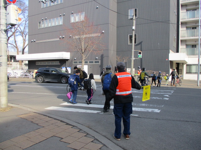 地域の方々が横断歩道に立ち、横断する小学生を見守っている様子