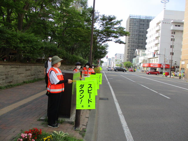 地域の方が北大正門前の歩道でスピードダウンの旗を持ち、啓発活動をしている様子