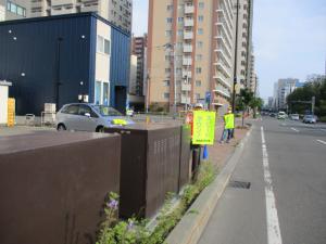 鉄西会館前でスピードダウンの旗を持ち、通り過ぎる自動車に安全運転を呼び掛けている様子