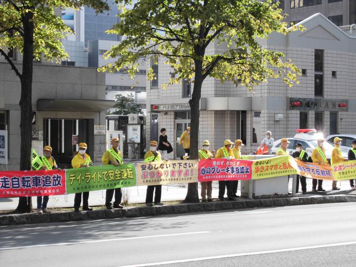 交通安全の横断幕を持って沿道で啓発をしている様子