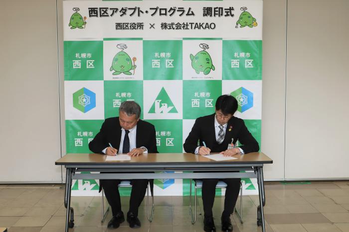 調印の様子（左：高尾代表取締役、右：村上西区長）