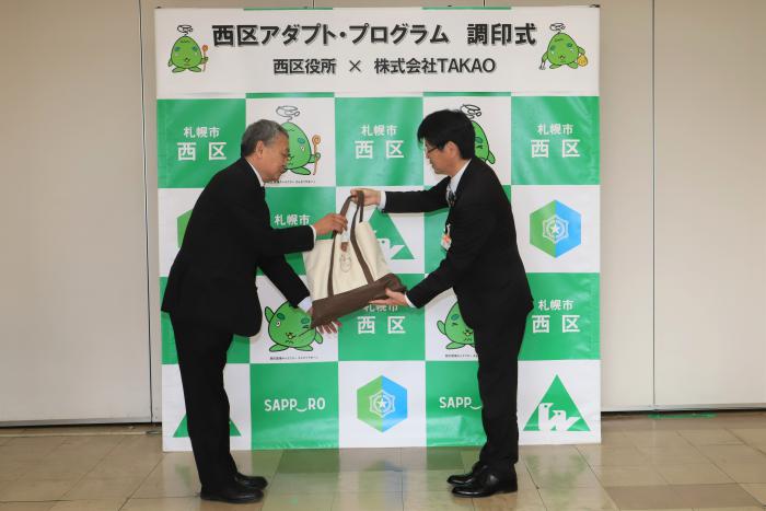 清掃用品贈呈の様子（左：高尾代表取締役、右：村上西区長）