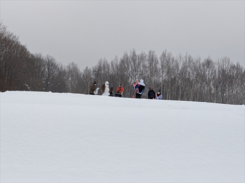 そり遊び場から離れた高いところで、雪で何かを作っている子どもと大人たち