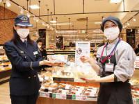 記念ロゴマーク入りシールが貼られた商品を持つ消防署員とイオン東札幌店員