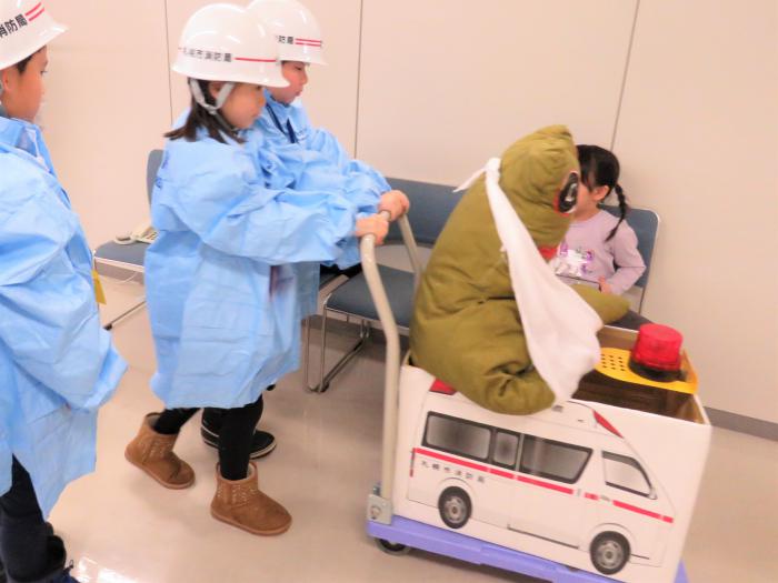 傷病者に見立てたカエル人形を段ボールで作った救急車に乗せて病院へ向かう様子