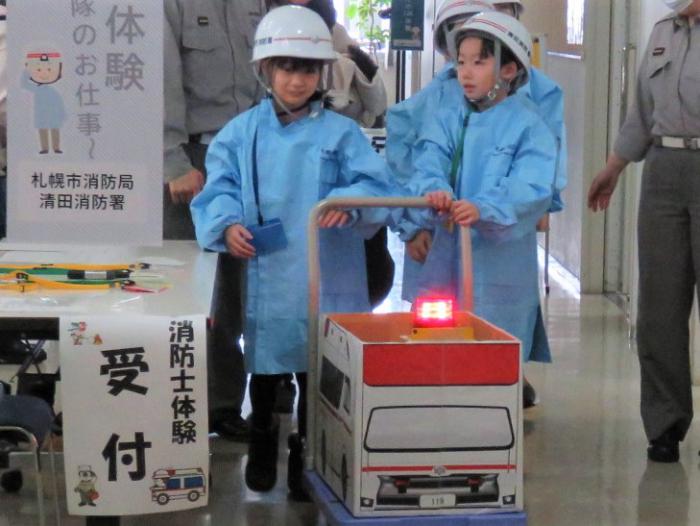 子どもたちがヘルメット等を身に着け、段ボールで作った救急車を動かして救急現場へ向かっている様子