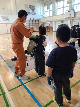 小学生が空気呼吸器を背負い重さを体験している様子