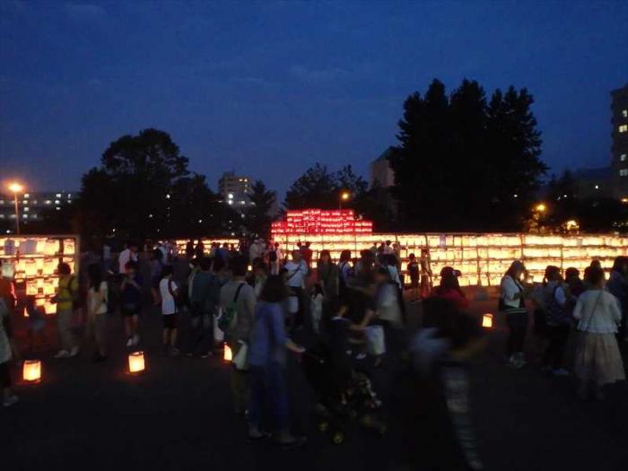 夏あかりの会場である、てっぽく広場に設置した、多数の提灯に火を灯して、多くの来場者が見入る様子を写した画像