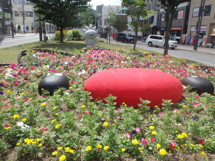 手稲駅前ロータリーに設置された、ていぬの直立姿勢の石像の前に作られた、ていぬ型の花壇に咲く花の画像