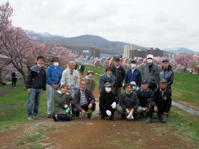 写真：こいのぼりと桜を背景に、やりがいに満ちた素敵な笑顔の「軽川と桜並木を育てる会」のみなさん。