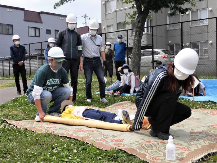 毛布をくるんだ両端に棒を巻き付けた簡易的な担架で訓練する町内会の担当者